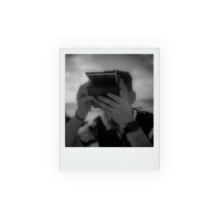 a black and white polaroid photo of a bearded man holding a polaroid camera