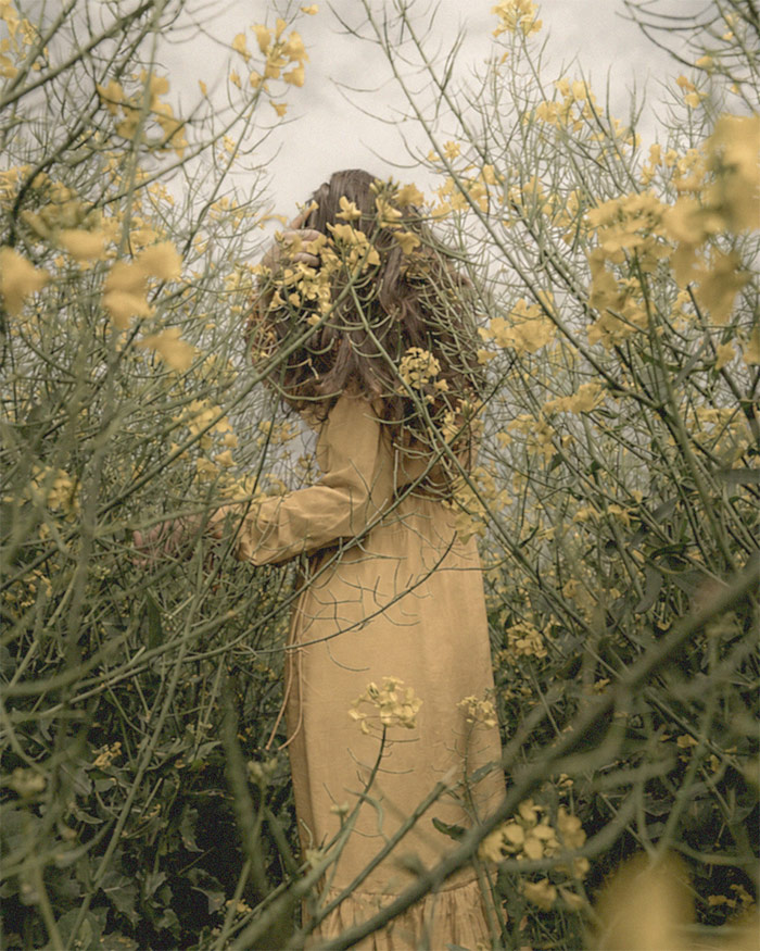 a woman walks through overgrown field while flowers begin to bloom around her as a symbol of good luck
