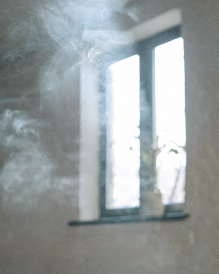 a smoke cleansing ritual takes place in an apartment with a white brick wall and black frame window