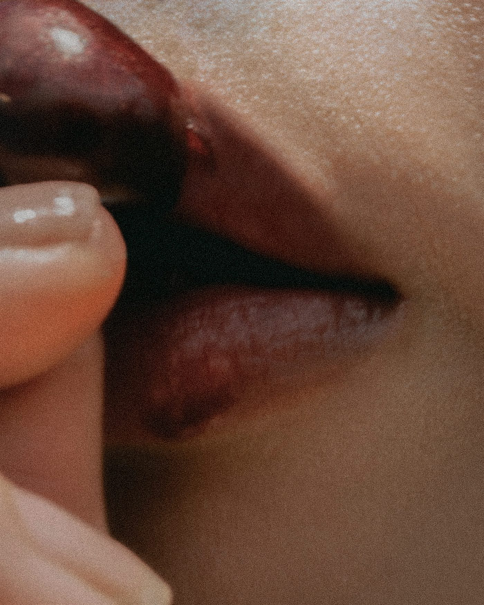 a cherry is pressed on lips stained in a deep red attracting a better kisser