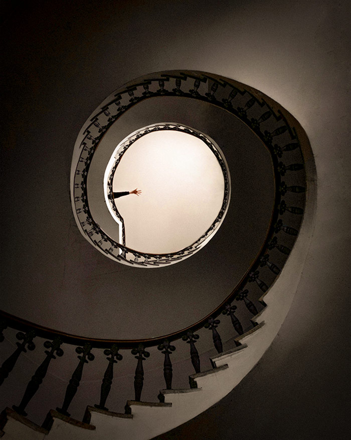 a hand waves at the top of a large spiral staircase